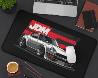 May include: Black rectangular mousepad featuring a white sports car illustration with the text "JDM" in red and white. The mousepad is on a black surface with a laptop, coffee cup, and stationery.