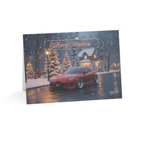 以下が含まれることがあります： 雪景色の中に赤いスポーツカーが描かれたクリスマスカード。カードには「Merry Christmas」の文字が装飾バナーで表示されています。車にはクリスマスのリースが飾られています。雪に覆われた木々も描かれています。