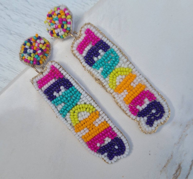 May include: A pair of colorful beaded earrings with the word "Peace" spelled out in rainbow colors. The earrings are made with small, colorful beads and have a gold-colored wire frame.