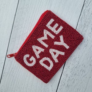 Pu&ograve; includere: Portafoglio rosso con cerniera a forma di perline con le parole "GAME DAY" in perline bianche.
