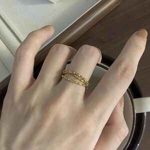 Puede incluir: Un anillo dorado con tres filas de cuentas ovaladas conectadas.