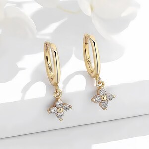 Puede incluir: Pendientes de aro de oro con un colgante de flor que presenta piedras de circonita cúbica transparentes.