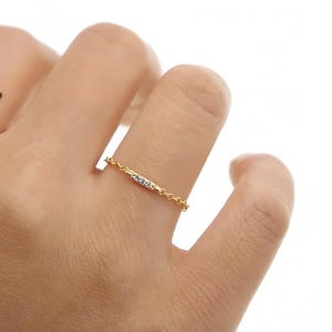 Puede incluir: Un delicado anillo de cadena de oro con una pequeña fila de piedras de circonita cúbica transparentes.