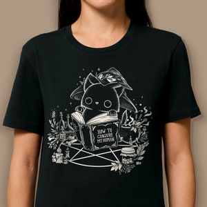 人間を召喚する方法 - 100%オーガニックコットン製の黒のユニセックスTシャツ - 魔法の本を持った黒い魔女猫
