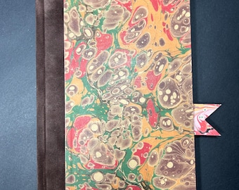 May include: A handmade journal with a brown suede spine and a colourful marbled cover. The cover features a pattern of red, green, and brown swirls on a yellow background. A decorative bookmark is inserted.