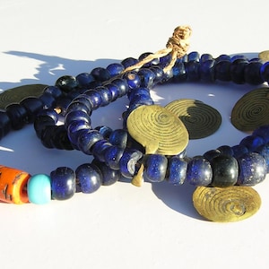 Könnte beinhalten: Ein Set aus drei blauen Glasperlenketten mit goldenen Metallakzenten. Die Ketten sind übereinander gelegt und haben verschiedene Perlengrößen und -formen.