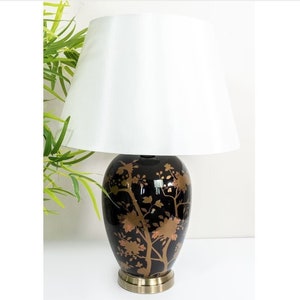 May include: A black ceramic table lamp with a white lampshade. The lamp base features a gold floral design.