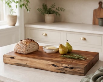 May include: A rectangular wooden cutting board with a natural live edge, featuring a loaf of crusty bread, a small white ceramic dish containing a square of butter, two green pears, and a sprig of fresh rosemary arranged on its surface.