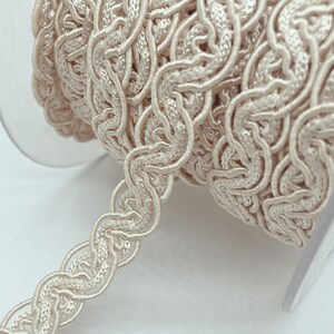 May include: A spool of ivory-colored braided trim with a delicate, intricate pattern. The trim is made of a soft, flexible material and is perfect for adding a touch of elegance to any project.