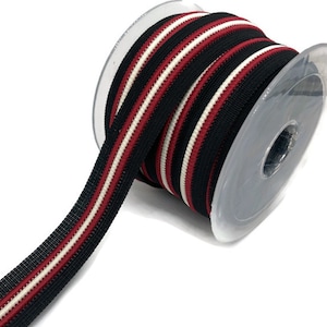 May include: A spool of black, white and red striped elastic ribbon. The ribbon is wound around a clear plastic spool.