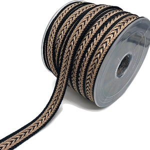 Op de afbeelding: Een rol decoratief lint met een zwart en goud chevronpatroon. Het lint is op een transparante plastic spoel gewikkeld, met een deel afgerold, dat het patroon laat zien. Ideaal voor knutselen en versieringen.