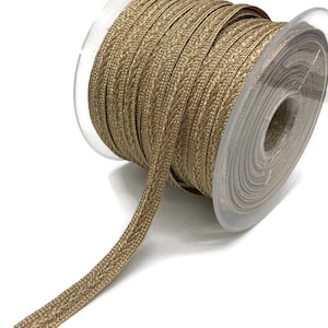 May include: A spool of gold metallic trim with a textured woven design. The trim is wound around a clear plastic spool.