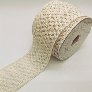 May include: A roll of off-white crocheted trim with a delicate floral pattern. The trim is rolled up on a cardboard spool.