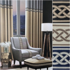 Puede incluir: Cortinas beige con un ribete trenzado gris y negro, un sillón gris con un ribete trenzado a juego, un pequeño puf con el mismo ribete y una lámpara blanca sobre un trípode de madera. Las cortinas están delante de una ventana con vistas a un horizonte urbano.