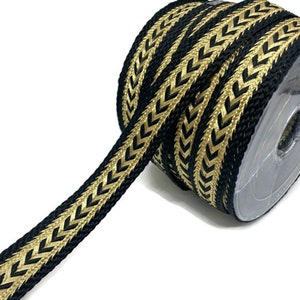 Puede incluir: Un rollo de ribete negro y dorado con un patrón de chevron. El ribete está tejido con un material texturizado, similar a una cuerda.