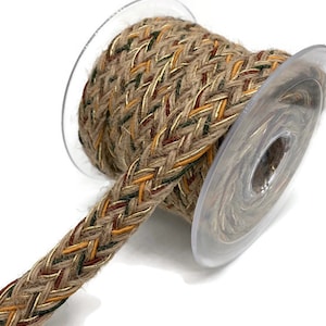 Könnte beinhalten: Eine Rolle geflochtenes Juteband mit goldenen, roten und grünen Akzenten. Das Band befindet sich auf einer Spule und ist bereit für Bastelarbeiten oder Dekorationen.