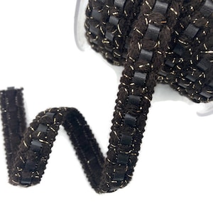 May include: Brown velvet trim with gold thread and black leather accents. The trim is woven and has a decorative stitch pattern.