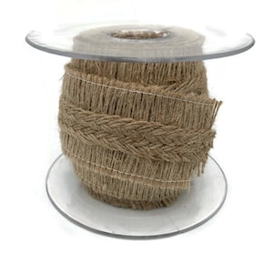 May include: A spool of natural jute ribbon with a braided design and fringed edges. The ribbon is a light brown color and is wound around a clear plastic spool. This decorative ribbon is suitable for crafts and gift wrapping.