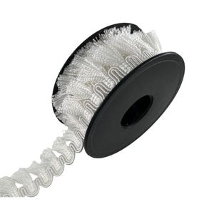 May include: A spool of white fringe trim with a decorative looped edge. The trim is made of a soft, textured material and is wound around a black plastic spool. The fringe is approximately 1 inch wide, perfect for sewing and craft projects.