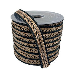 May include: A spool of decorative ribbon with a black base and a gold chevron pattern. The ribbon is tightly wound on a plastic spool, with a length of ribbon extending from the top. The ribbon is suitable for crafts and sewing projects.