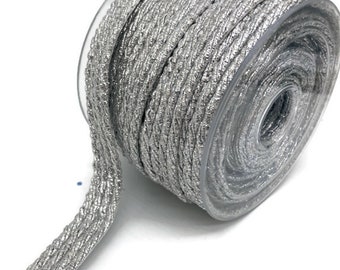 Puede incluir: Una bobina de ribete trenzado metálico plateado. El ribete es de color plateado, tejido, texturizado y brillante.