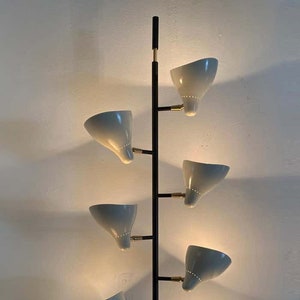 Könnte beinhalten: Eine schwarze Wandleuchte mit sechs weißen Lampenschirmen. Die Lampenschirme sind abgewinkelt und haben ein kleines Loch in der Mitte. Die Leuchte hat eine schwarze Metallstange mit goldenen Akzenten.
