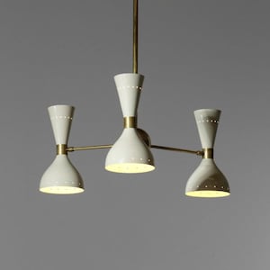 Op de afbeelding: Een messing en witte kroonluchter met drie lampen. De kroonluchter heeft een modern ontwerp met een geometrische vorm.
