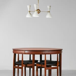 Op de afbeelding: Een ronde houten eettafel met vier stoelen. De tafel heeft een donkerhouten afwerking en de stoelen hebben zwarte leren zittingen. Een witte en gouden kroonluchter hangt boven de tafel.