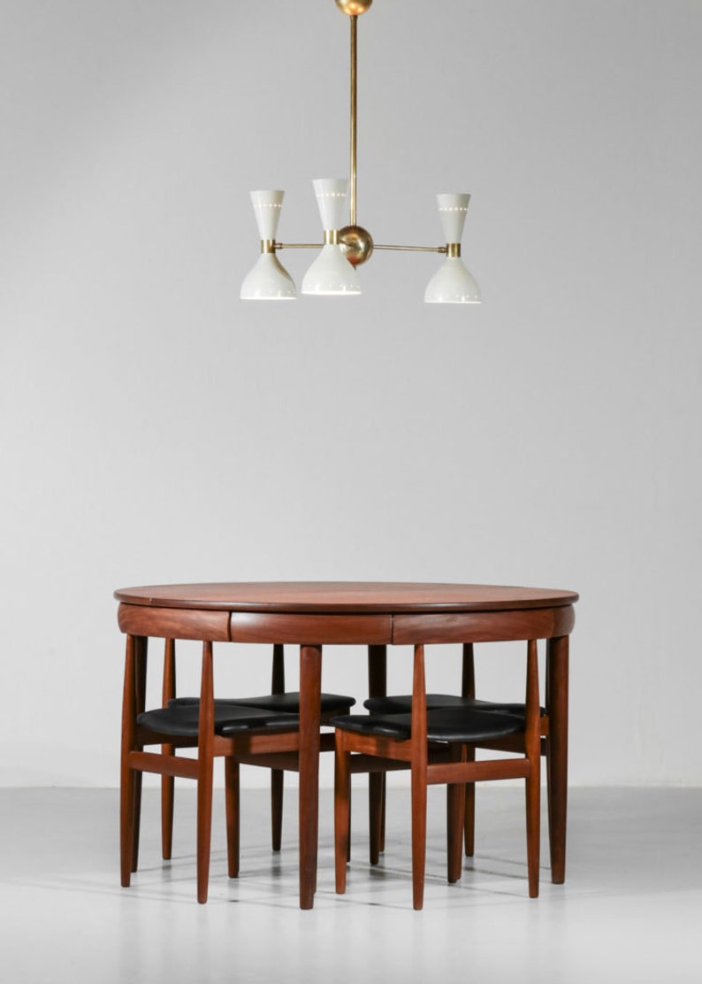 Op de afbeelding: Een ronde houten eettafel met vier stoelen. De tafel heeft een donkerhouten afwerking en de stoelen hebben zwarte leren zittingen. Een witte en gouden kroonluchter hangt boven de tafel.