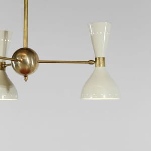Op de afbeelding: Een messing en witte kroonluchter met vier lichten. De kroonluchter heeft een centrale bol en drie armen die naar buiten uitstrekken met een licht aan het einde van elke arm.