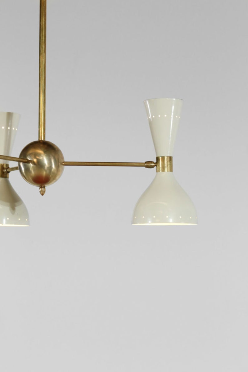 Op de afbeelding: Een messing en witte kroonluchter met vier lichten. De kroonluchter heeft een centrale bol en drie armen die naar buiten uitstrekken met een licht aan het einde van elke arm.