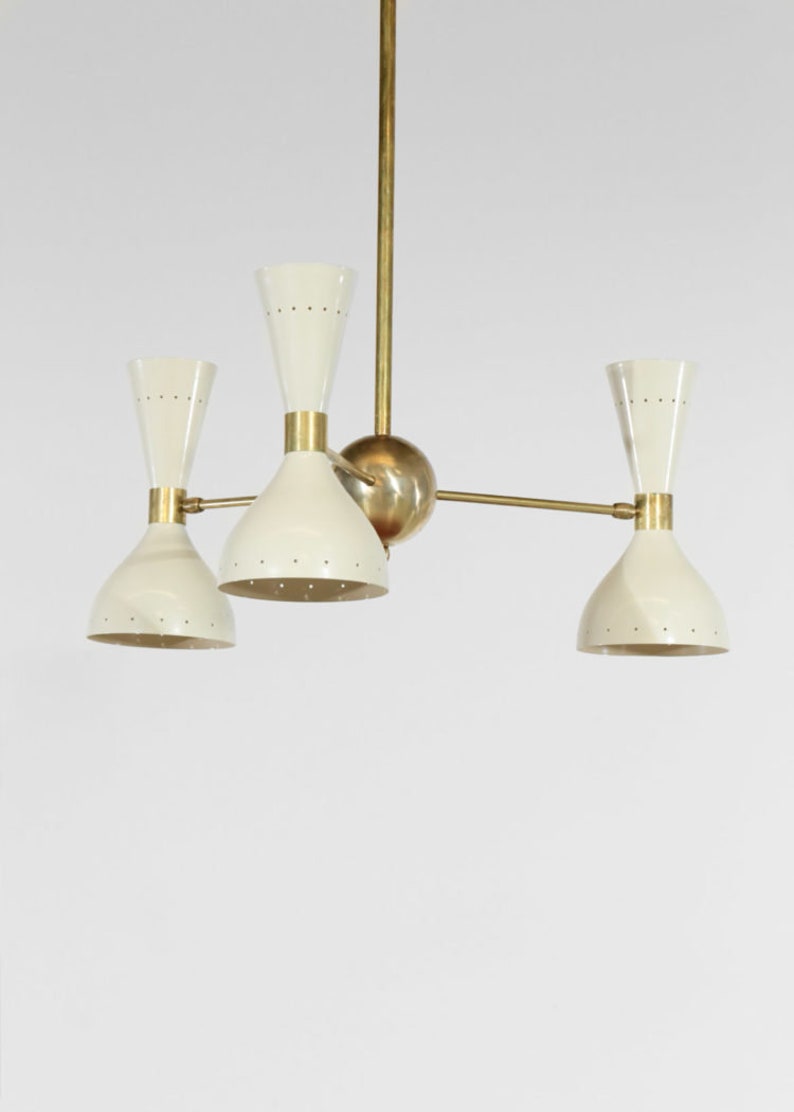 Op de afbeelding: Een messing en witte kroonluchter met vier lichten. De kroonluchter heeft een centrale messing bol en drie armen die naar de lichten uitstrekken. Elk licht heeft een witte, klokvormige kap met een messing bovenkant.