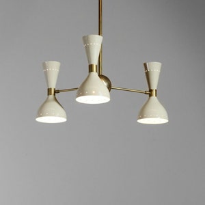Op de afbeelding: Een messing en witte kroonluchter met drie lampen. De kroonluchter heeft een modern ontwerp met een eenvoudige, geometrische vorm.
