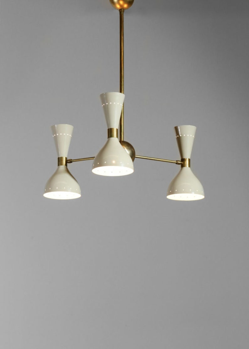 Op de afbeelding: Een messing en witte kroonluchter met drie lampen. De kroonluchter heeft een modern ontwerp met een eenvoudige, geometrische vorm.