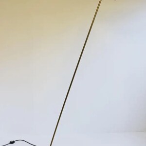 May include: A brass floor lamp with a black and white adjustable shade. The lamp has a round base and a long, slender arm.
