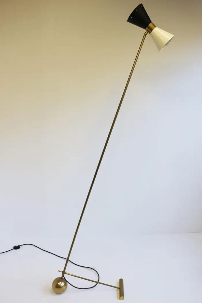 May include: A brass floor lamp with a black and white adjustable shade. The lamp has a round base and a long, slender arm.