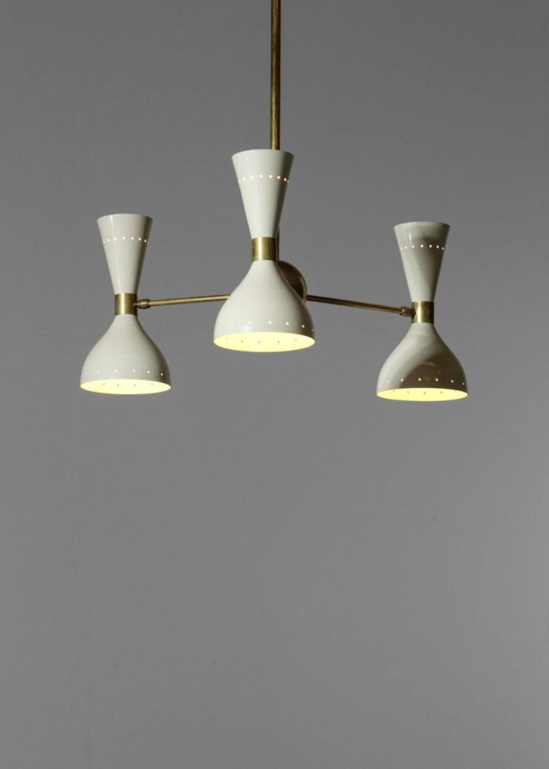 Op de afbeelding: Een messing en witte kroonluchter met drie lampen. De kroonluchter heeft een modern ontwerp met een geometrische vorm.