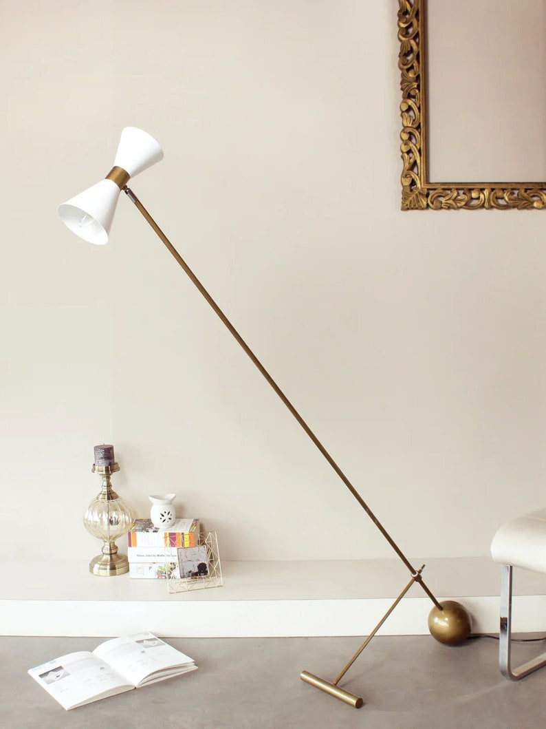 May include: A gold floor lamp with a white, double-trumpet shaped shade. The lamp has a long, thin arm and a round base.