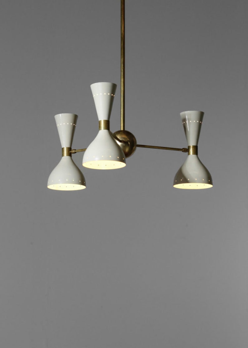 Op de afbeelding: Een messing en witte kroonluchter met vier lampen. De kroonluchter heeft een modern ontwerp met een centrale steel en drie armen die naar buiten uitstrekken. Elke arm heeft een witte, klokvormige kap met een kleine, ronde opening aan de bovenkant.
