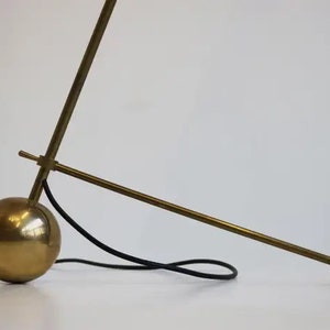 May include: A brass floor lamp with a round base and a long, adjustable arm. The lamp has a black cord.