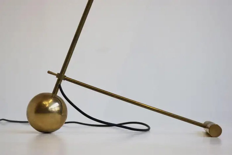 May include: A brass floor lamp with a round base and a long, adjustable arm. The lamp has a black cord.