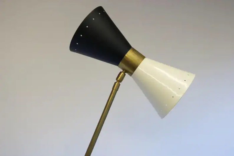 May include: A black and white adjustable floor lamp with a brass stem and a cone-shaped shade. The shade has a pattern of small holes.