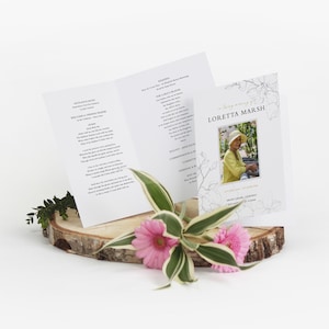 May include: A white memorial service booklet with a floral design and the name "Loretta Marsh" printed in gold. The booklet includes the order of service, readings, and a photograph of Loretta.