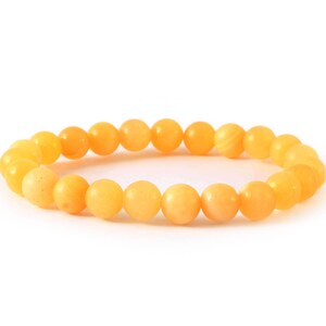 Op de afbeelding: Een armband met ronde, amberkleurige kralen. De kralen zijn geregen tot een doorlopende lus. De kralen hebben een gladde, gepolijste afwerking en variëren in kleur, van lichtgeel tot dieper amber. De armband is ontworpen om om de pols te worden gedragen.