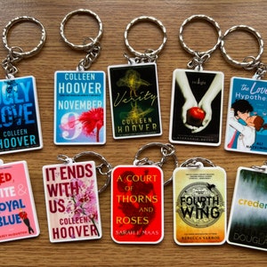 May include: Ten book-themed keychains featuring covers from popular novels. The keychains are white with colourful book covers. The titles include "Ugly Love", "November 9", "Verity", "Twilight", "The Love Hypothesis", "Red, White & Royal Blue", "It Ends With Us", "A Court of Thorns and Roses", "Fourth Wing", and "Credence".