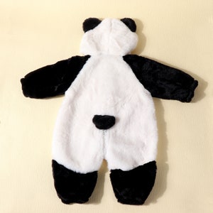 May include: A plush panda bear costume for a baby or toddler. The one-piece outfit features a white body with black accents on the arms, legs, and ears. A zipper runs down the front. The costume is designed to be worn as a hooded jumpsuit.