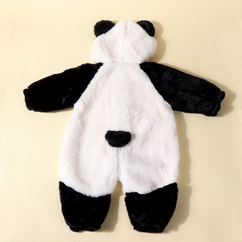 May include: A plush panda bear costume for a baby or toddler. The one-piece outfit features a white body with black accents on the arms, legs, and ears. A zipper runs down the front. The costume is designed to be worn as a hooded jumpsuit.