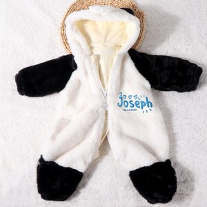 May include: A plush, white and black panda-themed baby jumpsuit with a hooded design. The jumpsuit features a full-length zipper and black accents on the sleeves and feet. The name "Joseph" and the date "Jan.14.2024" are printed in blue.
