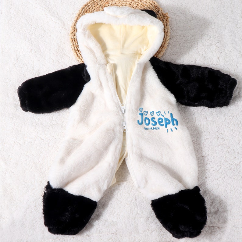 May include: A plush, white and black panda-themed baby jumpsuit with a hooded design. The jumpsuit features a full-length zipper and black accents on the sleeves and feet. The name "Joseph" and the date "Jan.14.2024" are printed in blue.