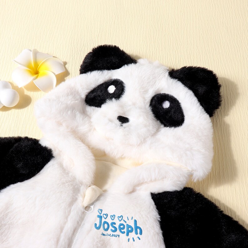 May include: A plush panda bear hooded jumpsuit in black and white with a zipper closure. The name "Joseph" and the date "Jan 1st, 2024" are embroidered in blue on the front. The jumpsuit has a soft, furry texture.